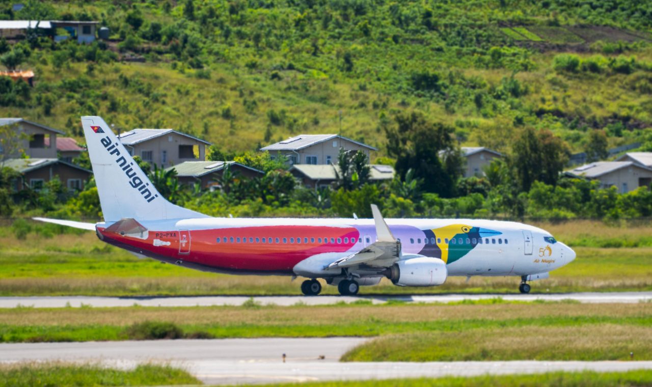 air niugini plane lands on runway with green landscape behind
